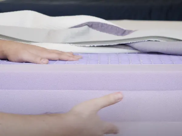 Close-up view of a hand pressing down on the Purple Mattress, showing its unique grid layer and foam construction.