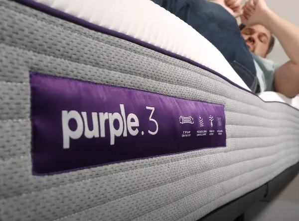 Close-up of a Purple .3 mattress label with a heavy person lying along the edge of the mattress, demonstrating strong edge support.