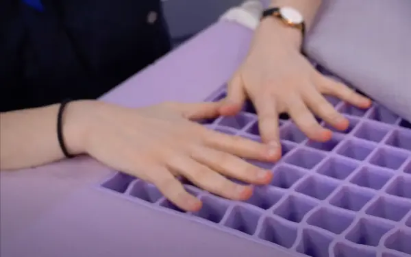 Close-up of a person’s hands pressing down on the Purple mattress grid layer, highlighting the flexible and supportive material.