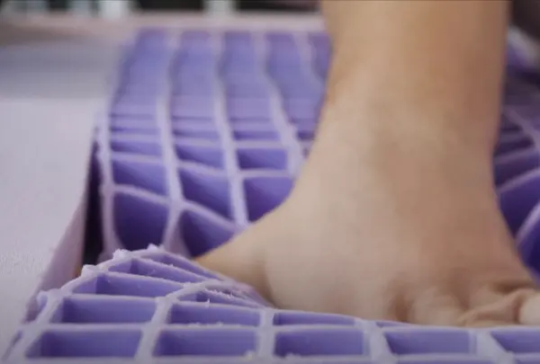 Close-up of a hand pressing down on the Purple mattress grid layer, highlighting the flexible and supportive material.