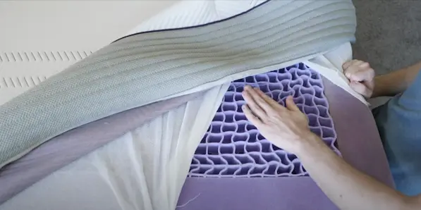 Close-up of a person's hand touching the Purple mattress's unique grid design, with the mattress cover partially lifted to reveal the internal structure in this Purple Mattress Review.