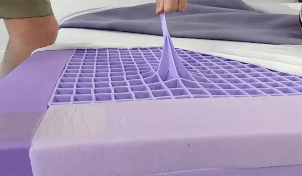 Close-up of a person stretching the Purple Mattress's grid layer, showcasing its flexibility and durability.