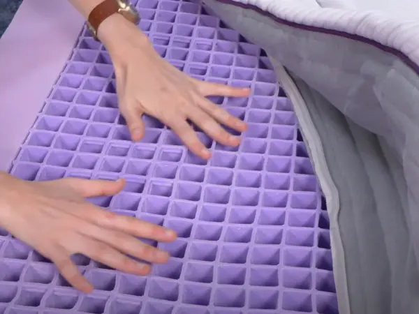 Hands pressing on the hyper-elastic polymer grid layer of a Purple mattress, revealing its unique design.