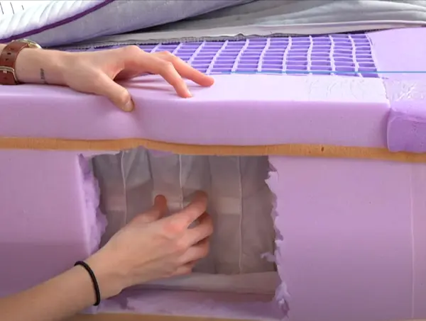 Hand showing the internal layers of a Purple mattress through a cutaway, highlighting the construction and materials.