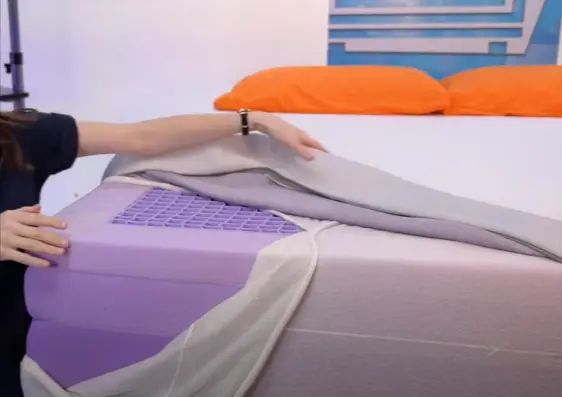 Person lifting the cover of a Purple mattress to reveal the grid layer and underlying foam structure, showcasing the mattress's design and build in this Purple Mattress Review.